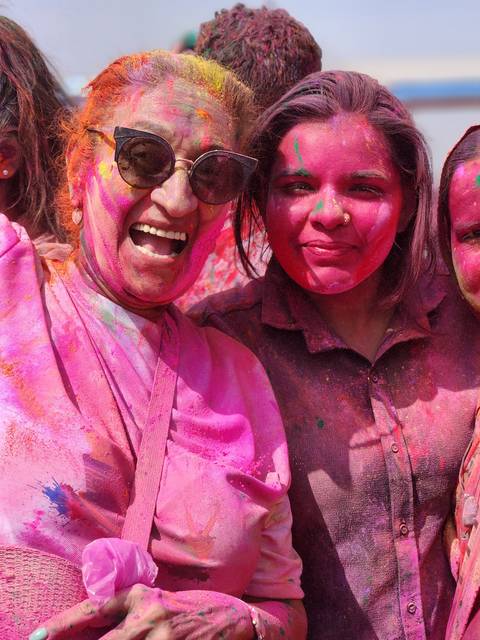 Two women with faces covered in colorful powder smiling.