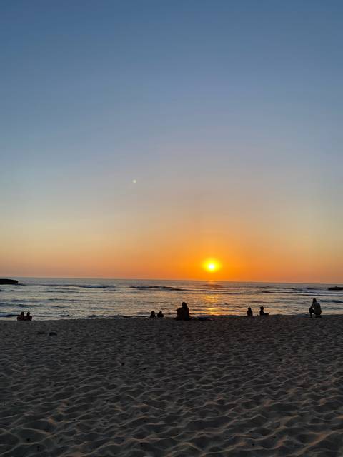 Sunset view over a sandy beach with silhouettes of people.