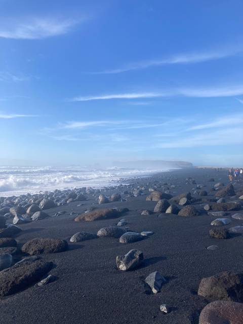 Rocky beach with waves and distant figures.