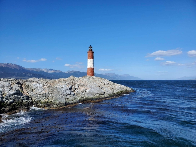 Lighthouse on a rocky shore with a mountainous backdrop.