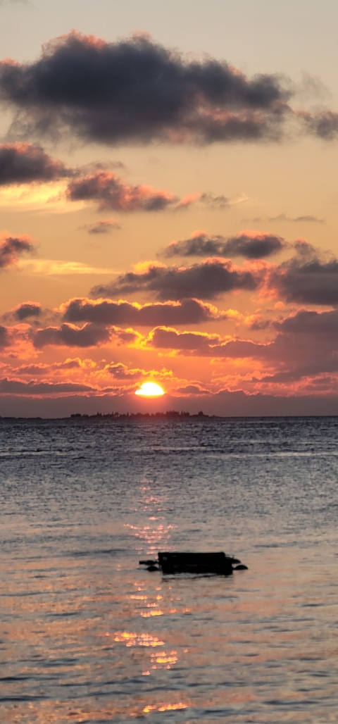       Sun setting over ocean with clouds in the sky.
  