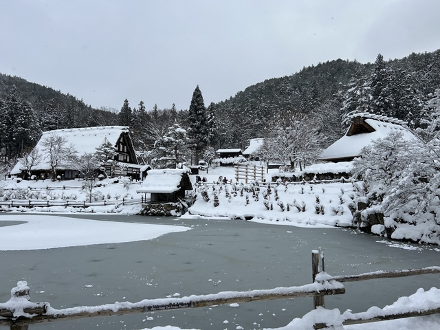 Snow-covered traditional houses by a frozen pond.