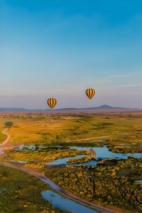       Two hot air balloons float over a vast open landscape during sunrise.
  