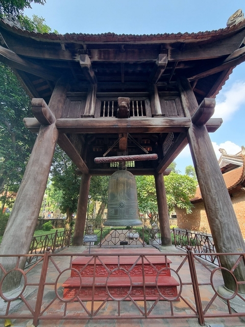 Historic bell in a wooden bell tower surrounded by trees.