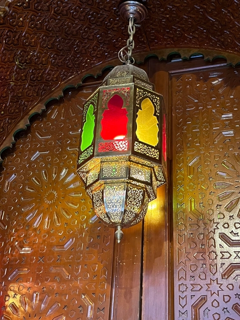 Decorative lantern with colorful panels hanging on an intricately designed wall.