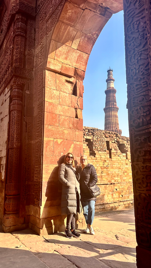       Two people posing in front of Qutub Minar.
  