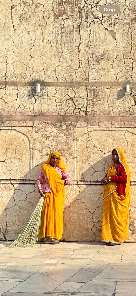       Two women in traditional attire standing against a textured wall.
  
