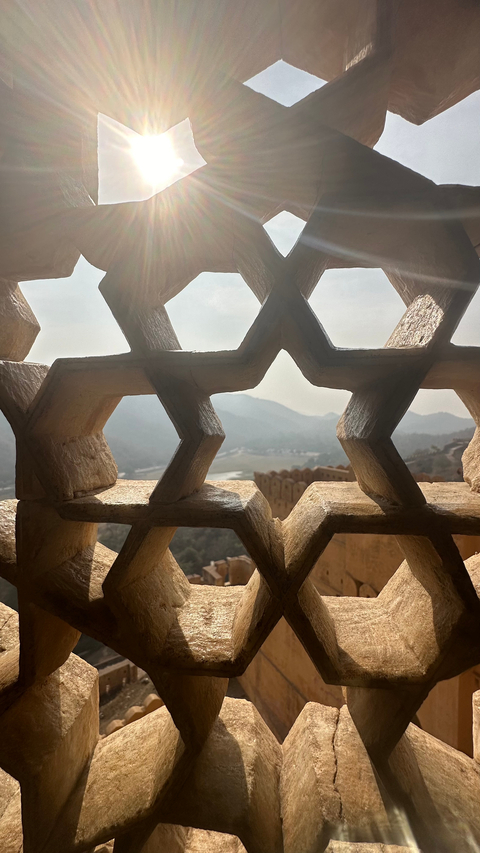       View through a patterned stone window showing distant hills.
  