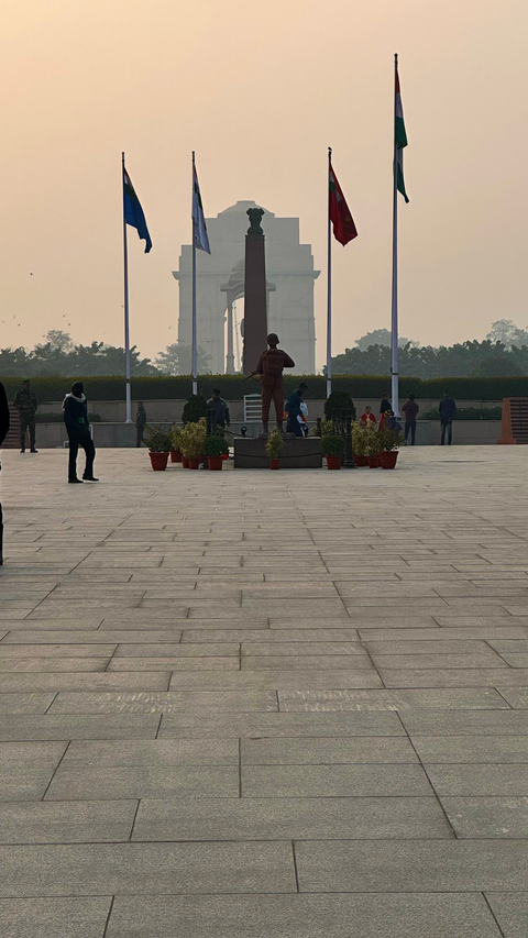       People walking in a square with a monument in the background.
  