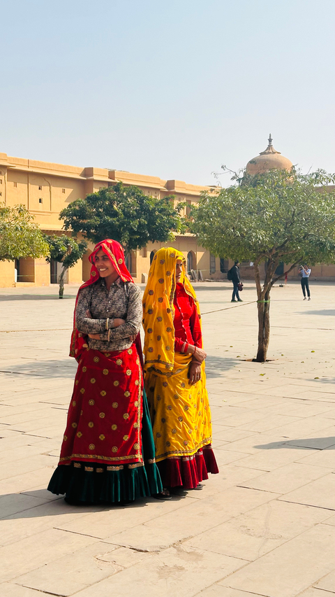       Two women in colorful saris smiling in a courtyard.
  