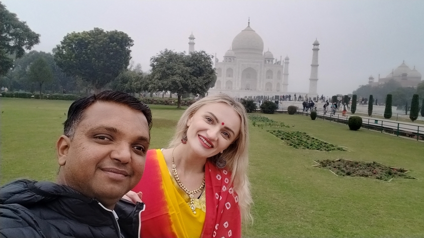 Two people smiling in front of the Taj Mahal on a foggy day.