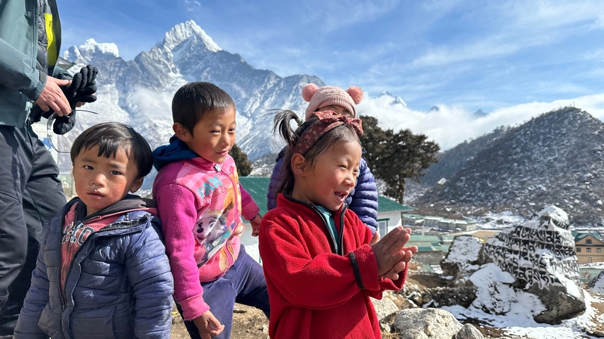 Group of children in colorful clothing with mountains in the background.