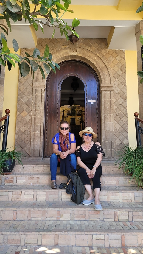       Two women sitting on steps in front of a large wooden door.
  