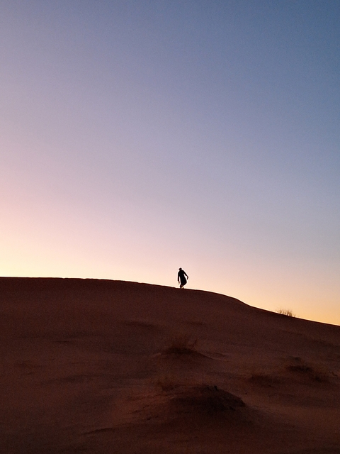 Silhouette of a person walking on a sand dune during sunset.
