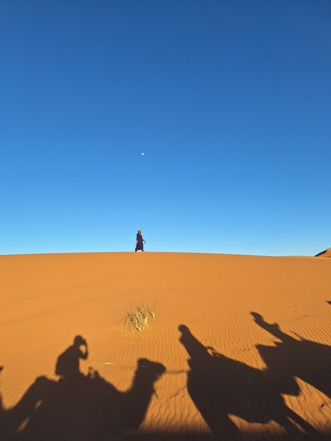 Individual walking atop a sand dune under a clear blue sky.