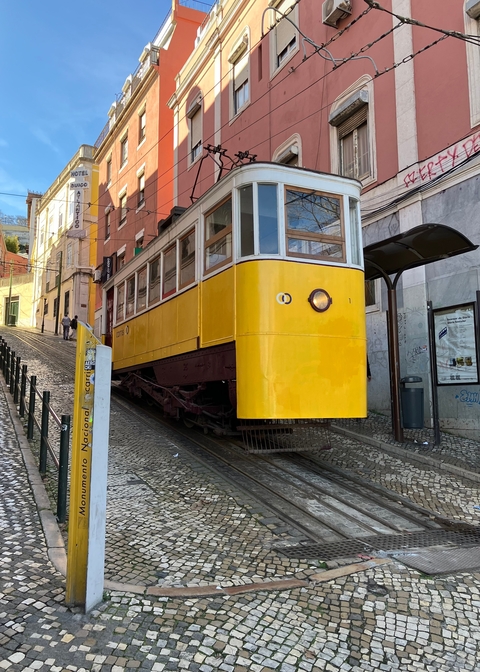       Yellow tram on a steep street with urban background.
  