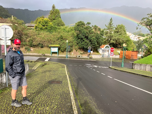       Person standing on a wet street with rainbow in the background.
  