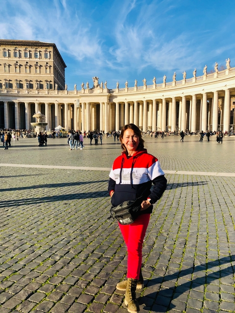       A smiling woman standing in an open square with architectural columns in the background.
  