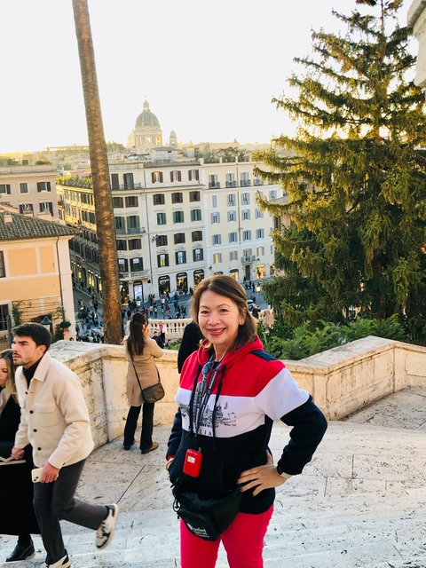      A woman standing on steps with city buildings in the background.
  