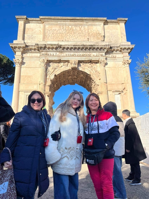       Three women posing in front of a triumphal arch.
  
