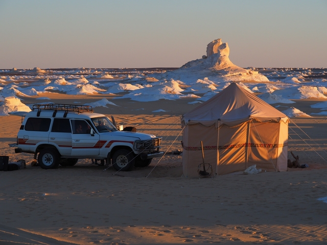 Sunset over a desert camp with a vehicle and tent.