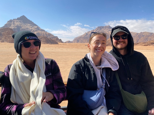       Three people posing with a desert landscape and rocky mountains in the background.
  