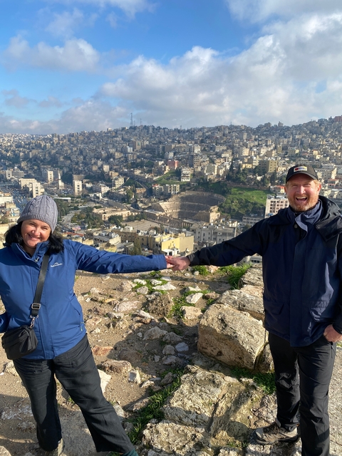 Two people posing with a cityscape view, including the Roman Theatre in the background.