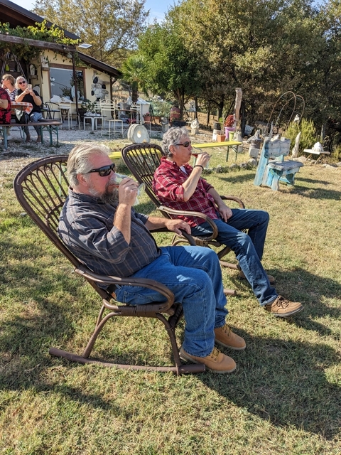       Two men sitting on chairs, drinking in a grassy outdoor setting.
  