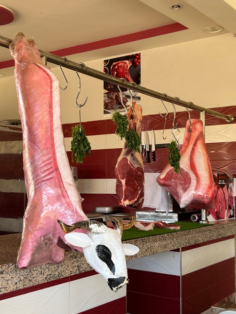 Butcher shop with meat cuts hanging, and herbs for sale.