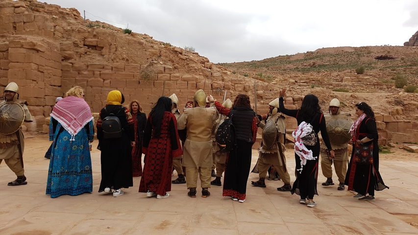       Group of people in traditional attire with historical rock structures in the background.
  