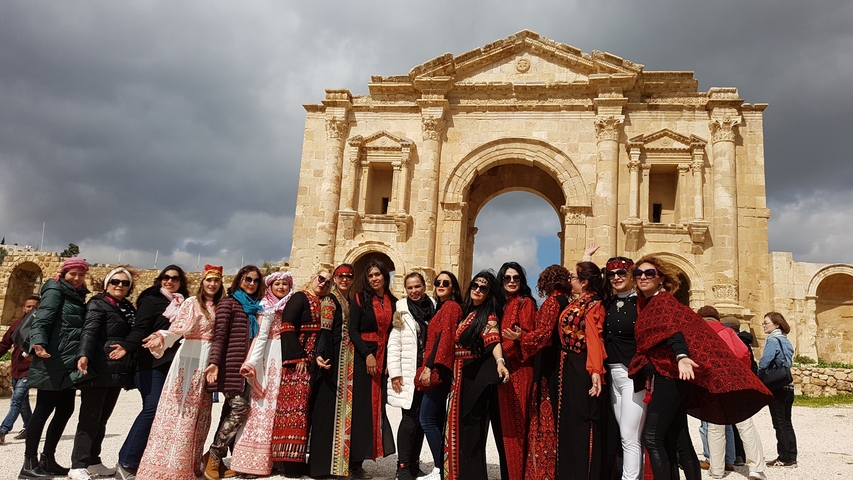       Group of women posing in front of an ancient stone archway.
  