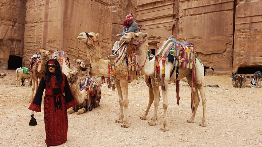       Woman posing next to camels in front of a rock-cut structure.
  