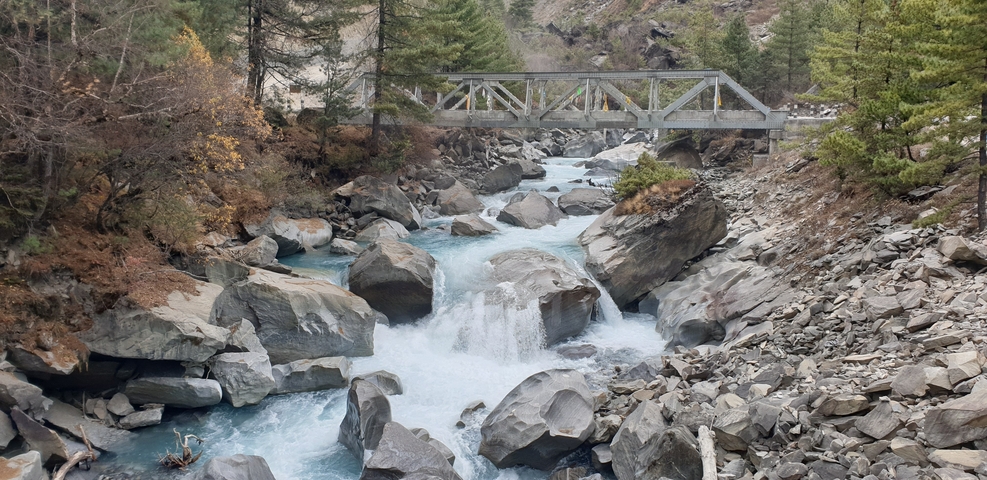 Mountain stream flowing under a bridge with rocky banks.