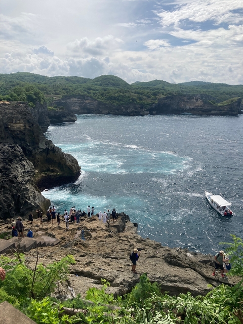       Tourists overlooking a rugged coastline with a boat.
  