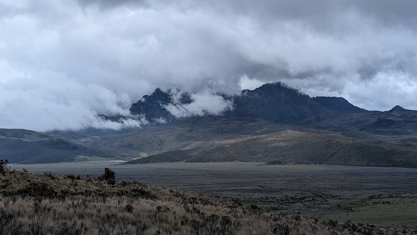       Cloud-covered mountains with grassland in foreground.
  