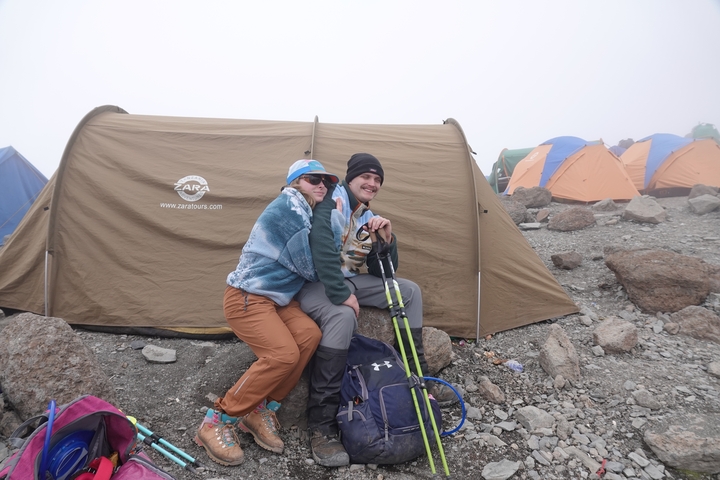       Two hikers in front of a tent in a mountainous area.
  