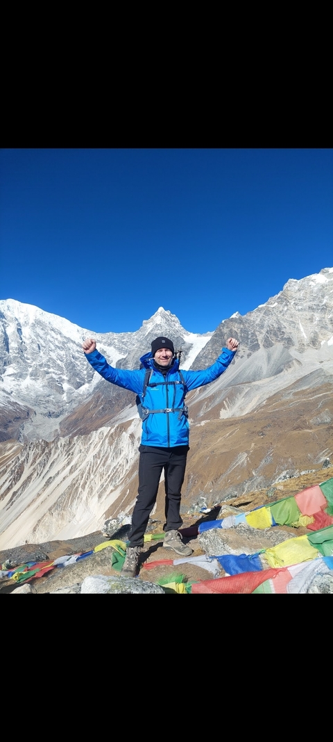 A man posing triumphantly in a mountain landscape.