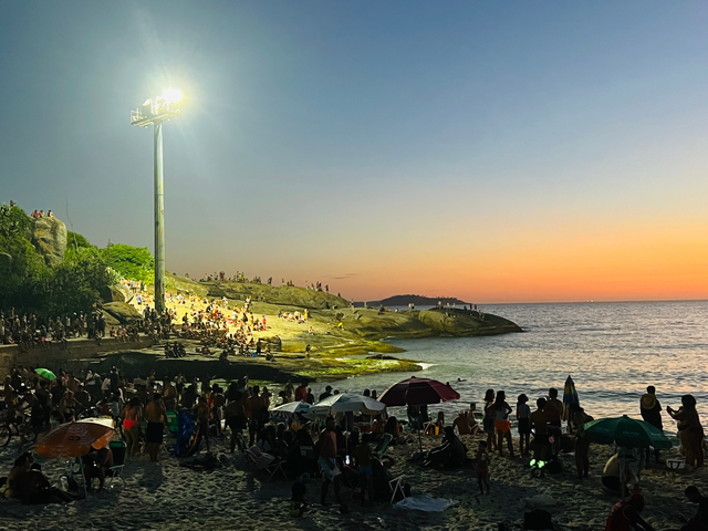 Crowded beach at sunset, people enjoying the view.
