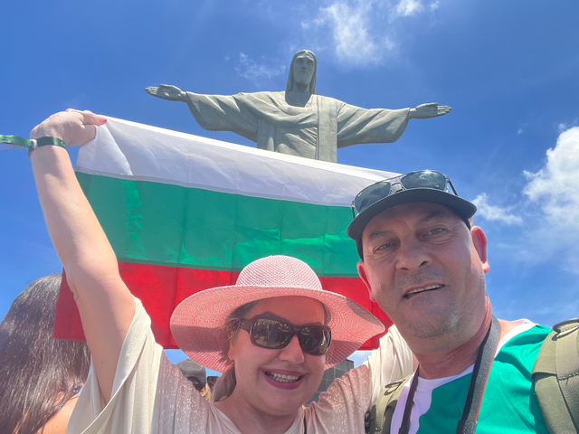 Tourists holding a flag, posing in front of Christ the Redeemer.