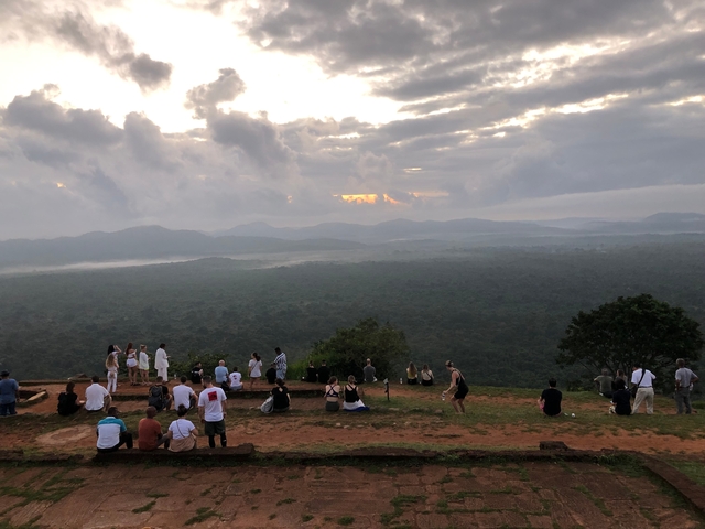       People gathered on a hilltop viewing a landscape at sunset.
  