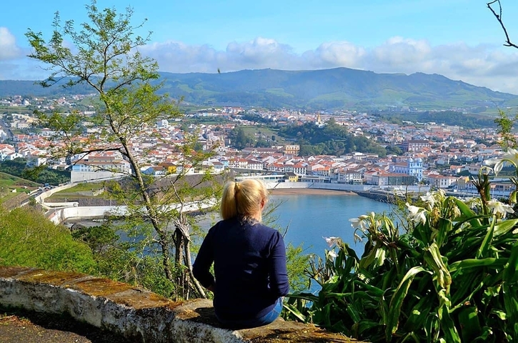 Person overlooking coastal town with mountains in the background.