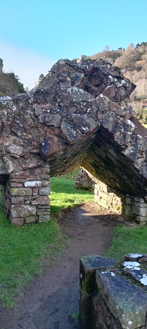       Close-up of an old stone archway ruins with grass beyond.
  