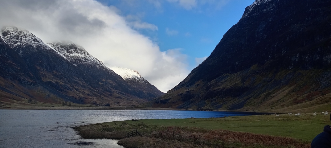       A scenic view of a lake surrounded by snow-capped mountains under a blue sky.
  