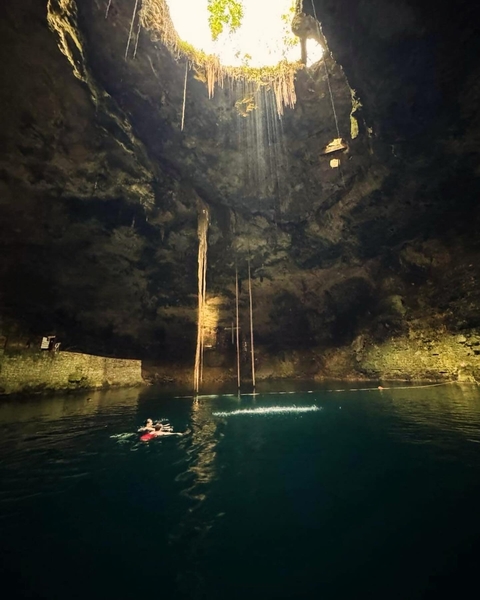       Swimmers in a cenote illuminated by natural light coming from above.
  