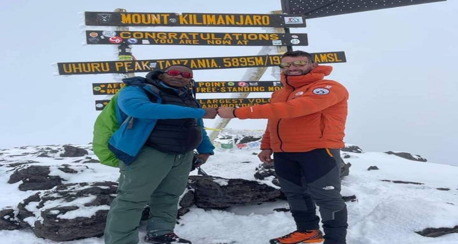 Two climbers fist-bumping near a sign on a snowy peak.