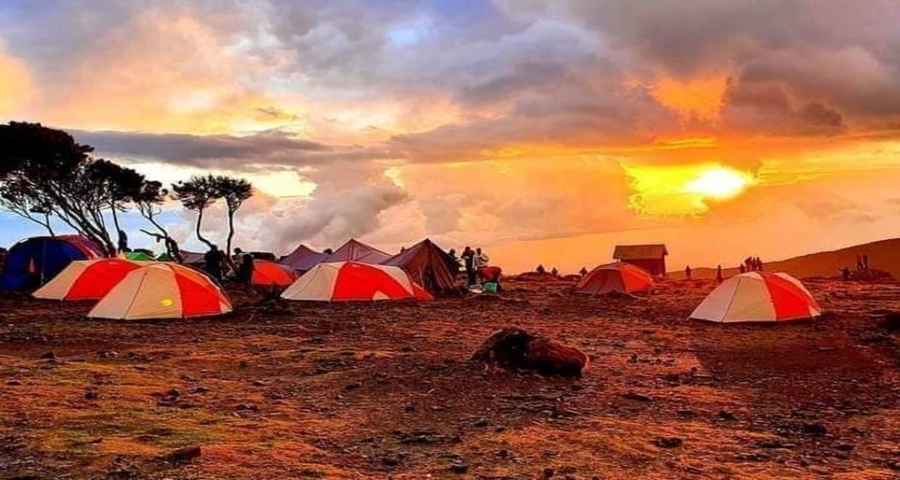 Colorful sunset over a camping site with orange tents.