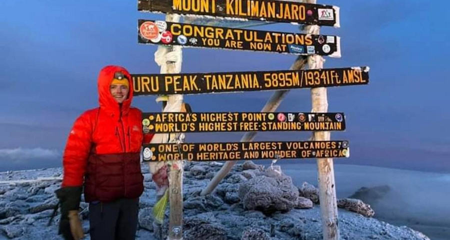 Climber posing beside a sign at a snowy summit.