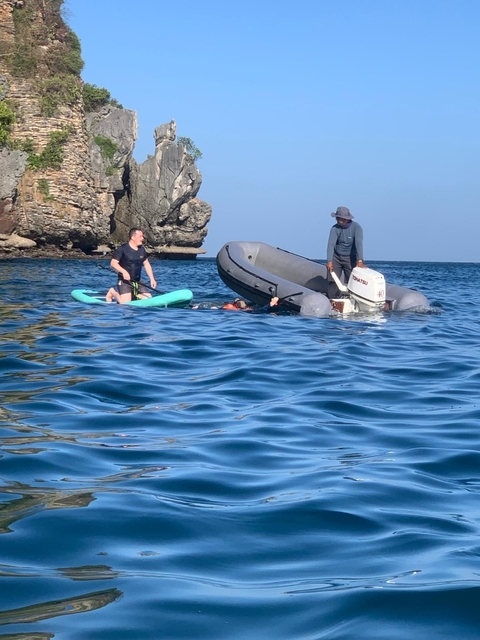 People in a small boat and on paddleboard in the sea.