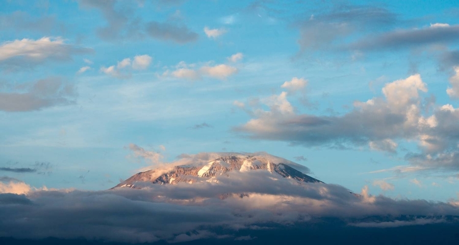 Distant view of snow-capped Mount Kilimanjaro beneath clouds.