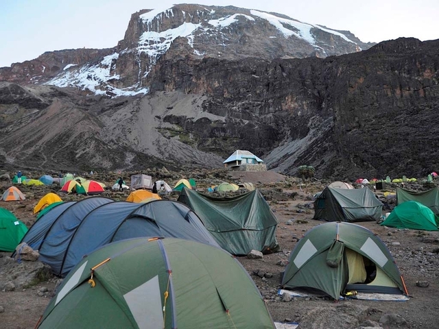 Camp site with colorful tents at the foot of a mountain.